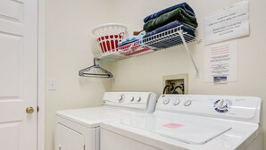 Un espace buanderie comprenant un lave-linge, un sèche-linge, un panier et une étagère avec des vêtements pliés.