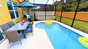 Ein Garten mit Swimmingpool, einem Esstisch mit Stühlen und einem Grill.