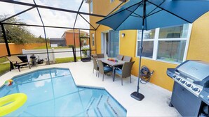 Ein Garten mit Swimmingpool, Grill, Esstisch und Stühlen sowie einem großen Sonnenschirm.