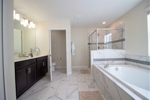A modern bathroom with a large mirror, a bathtub, and a shower area. - Champions Gate 8940 (Davenport)