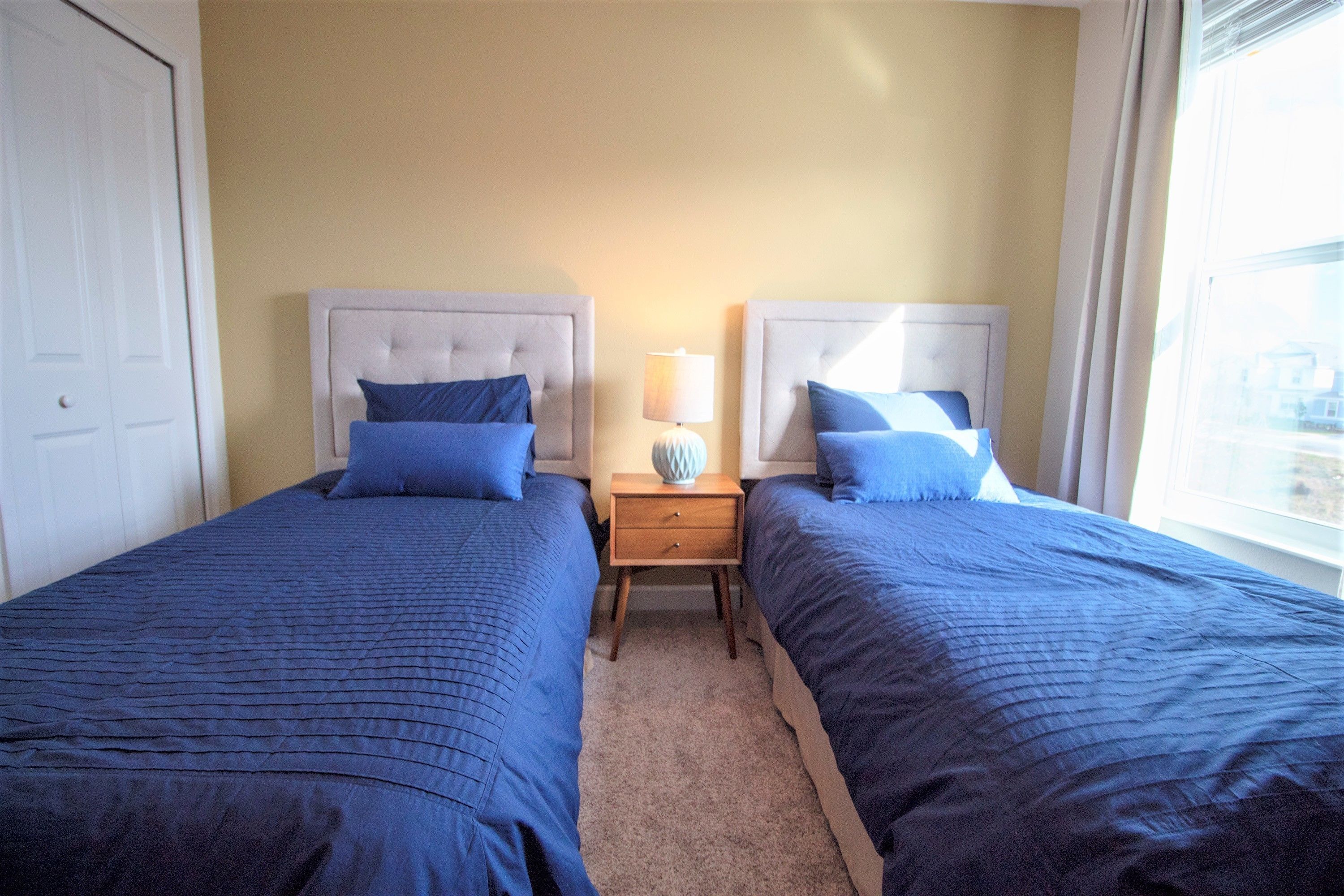 Una camera d'albergo con due letti, un comodino con una lampada e una finestra con tende.