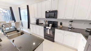 Uma cozinha moderna com armários brancos, micro-ondas preto, eletrodomésticos de aço inoxidável e bancada de granito.