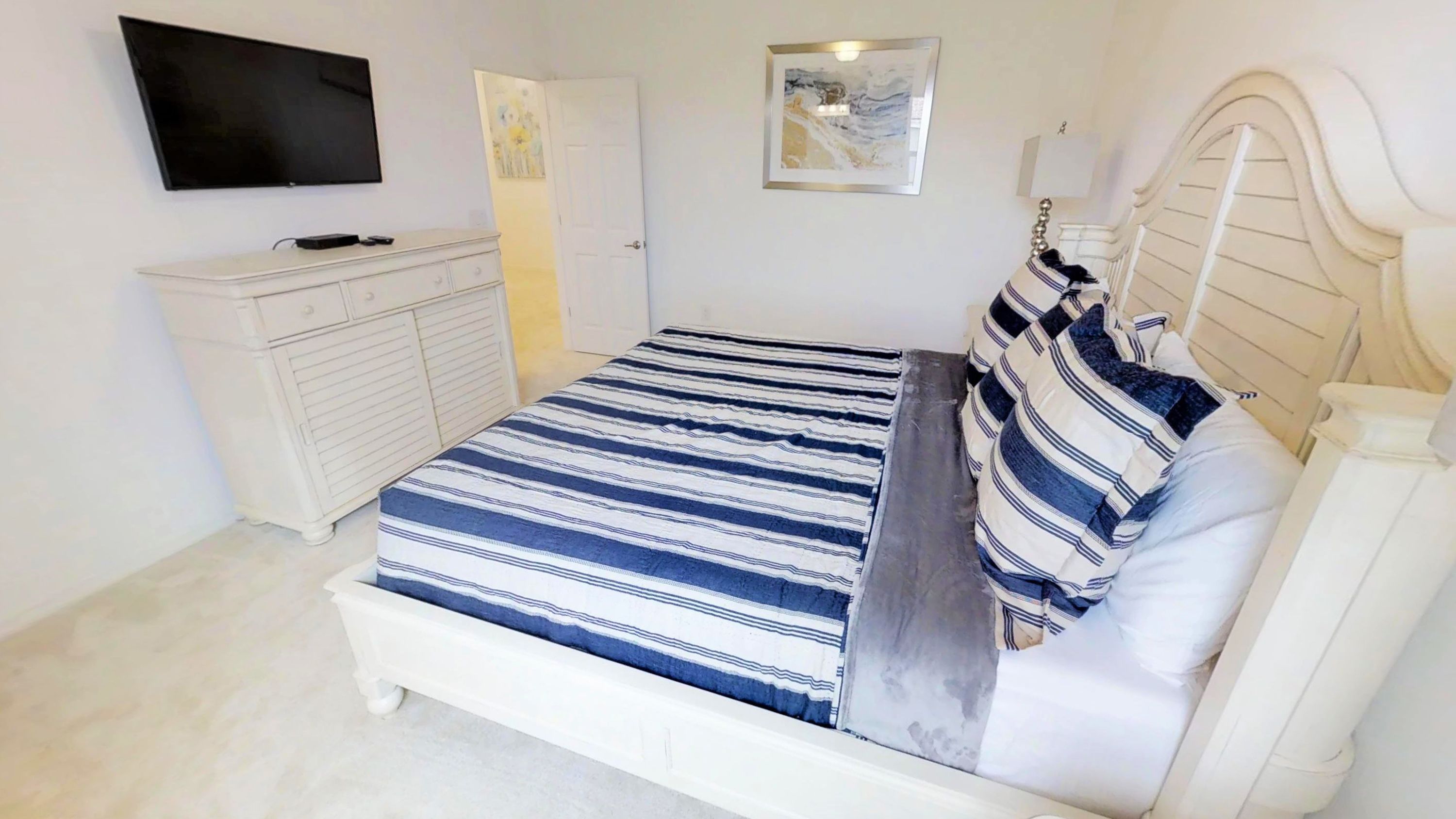 A bedroom with a bed, a dresser, a TV, and artwork on the walls.