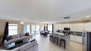 A modern kitchen with white cabinets, a central island with bar stools, and a dining area with a large table and chairs.