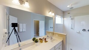 A modern bathroom with a large mirror, two sinks, a shower, and a camera on a tripod.