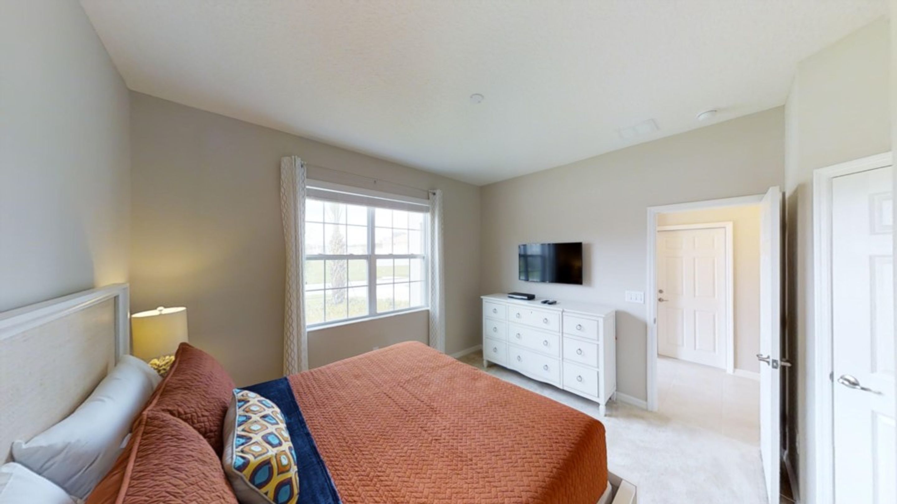 A bedroom with a bed, dresser, TV, and a door leading to another room.