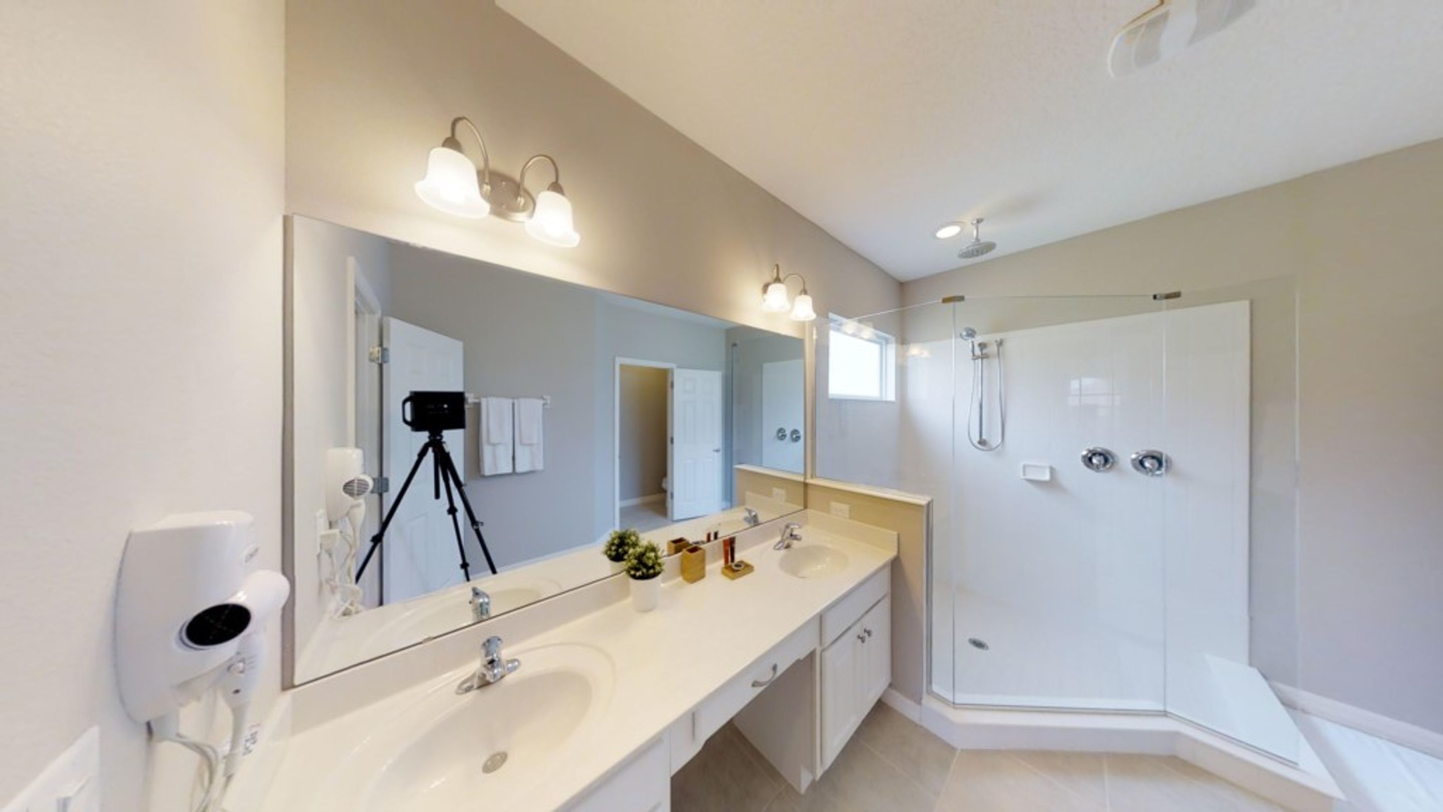 A modern bathroom with a large mirror, dual sinks, a shower, and a hairdryer.