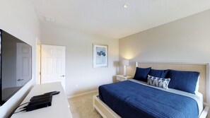 A bedroom with a bed, a desk with a computer, a TV, and a door.