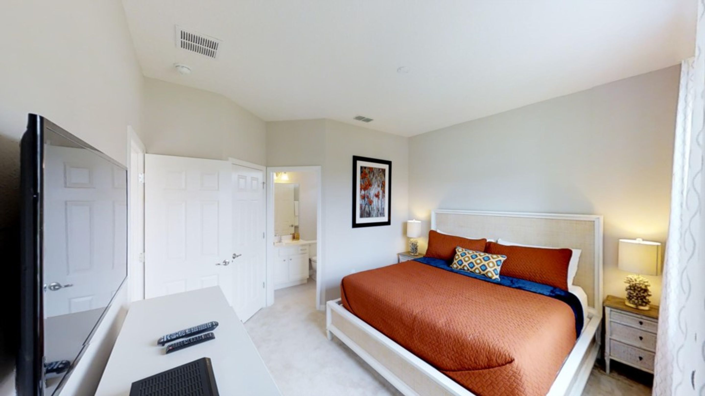 A bedroom with a bed, a desk, a television, and a mirror.