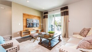 A living room with a wooden wall panel, a flat-screen TV, a coffee table, and a sofa. - Encore Resort at Reunion 7717 (Kissimmee)