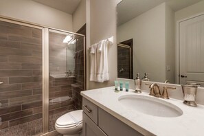 A modern bathroom with a glass shower enclosure, a white toilet, a vanity with a large sink, and a mirror. - Encore Resort at Reunion 7717 (Kissimmee)