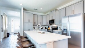 A modern kitchen with a large island, stainless steel appliances, and light-colored cabinetry. - Encore Resort at Reunion 7717 (Kissimmee)