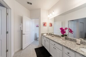 A modern bathroom with a large mirror, granite countertop, white cabinets, and a black rug. - Sonoma Resort 2692 (Kissimmee)