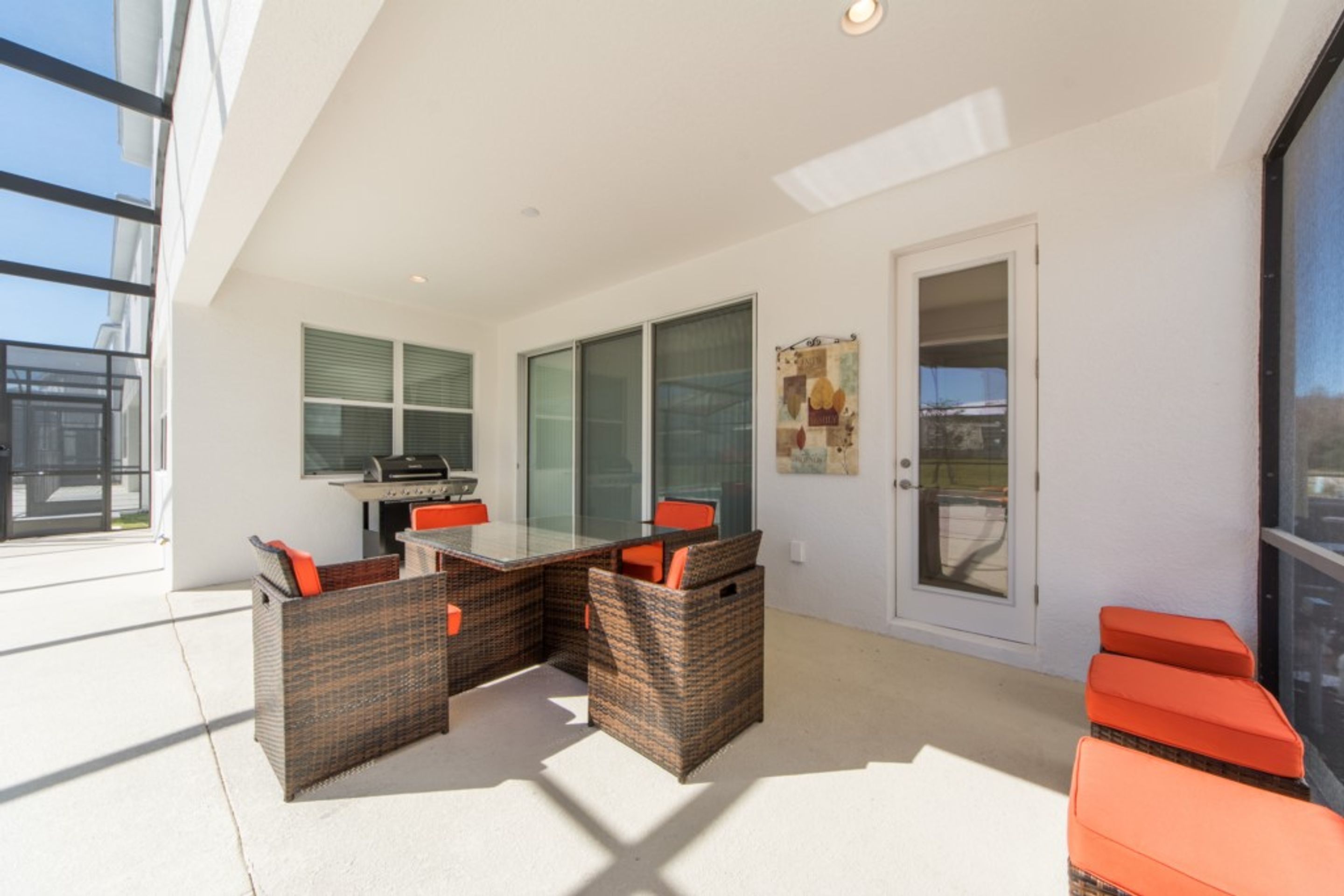 Une terrasse extérieure moderne, dotée d’une table en verre et de meubles en osier, d’une porte avec un panneau de verre et offrant une vue sur l’extérieur.