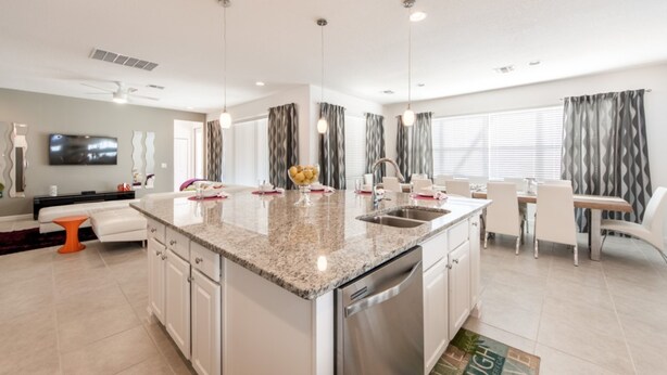 A modern kitchen with granite countertops, stainless steel appliances, and a dining area with white chairs and a table. - Sonoma Resort 2692 (Kissimmee)
