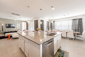 A modern kitchen with granite countertops, stainless steel appliances, and a dining area with white chairs and a table. - Sonoma Resort 2692 (Kissimmee)