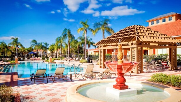 A resort pool area with lounge chairs, a water fountain, and palm trees. - Bella Vida 851 (Kissimmee)