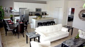 A modern kitchen with white cabinets, a central island, and a dining area with a white sofa and coffee table. - Bella Vida 851 (Kissimmee)