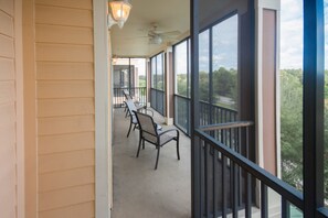 A covered outdoor area with a row of chairs and a table, large windows with a view of trees, and a ceiling fan. - Palisades Resort 14200 - 302 (Winter Garden)