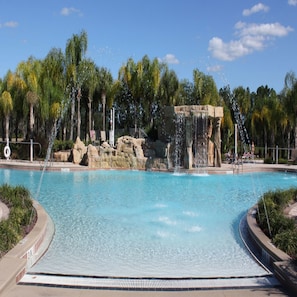 Ein Schwimmbecken mit klarem, blauem Wasser, umgeben von Palmen und einem Felswasserfall.