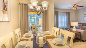 A dining area with a chandelier, dining table set for four, and a view of the outdoors. - Paradise Palms 2959 (Kissimmee)