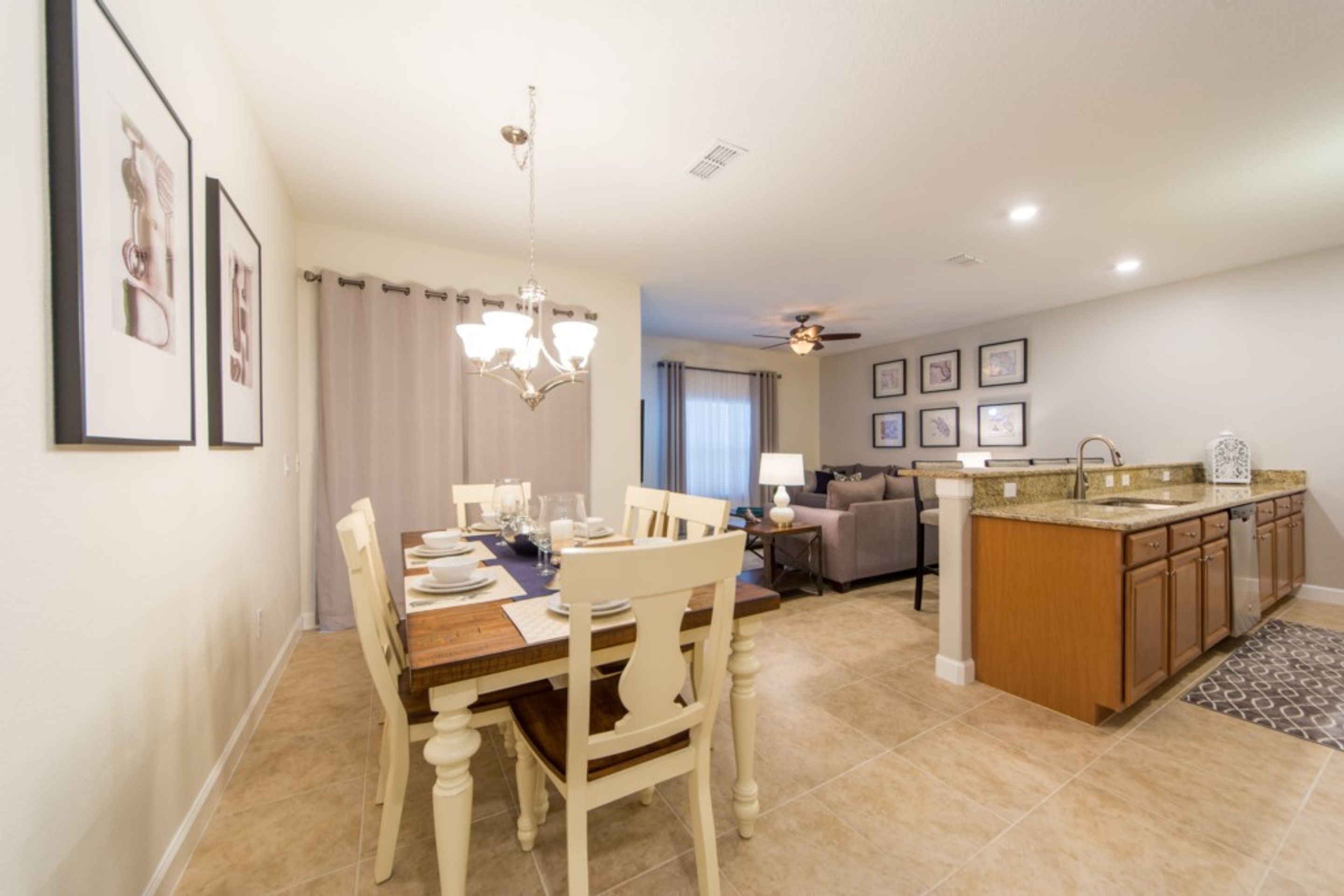 A dining area with a wooden table and chairs, a chandelier, and a kitchen with a granite countertop and wooden cabinets.