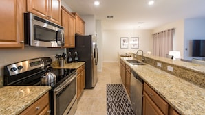 A modern kitchen with granite countertops, stainless steel appliances, wooden cabinets, and a built-in microwave. - Paradise Palms 2959 (Kissimmee)