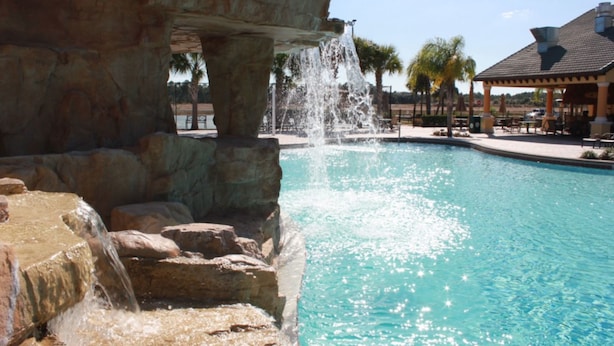 A pool with a waterfall feature, surrounded by stone structures and palm trees. - Paradise Palms 2959 (Kissimmee)