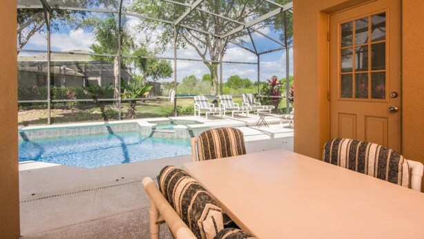 A covered patio with a pool, lounge chairs, and a table. - The Shire at West Haven 108 (Davenport)