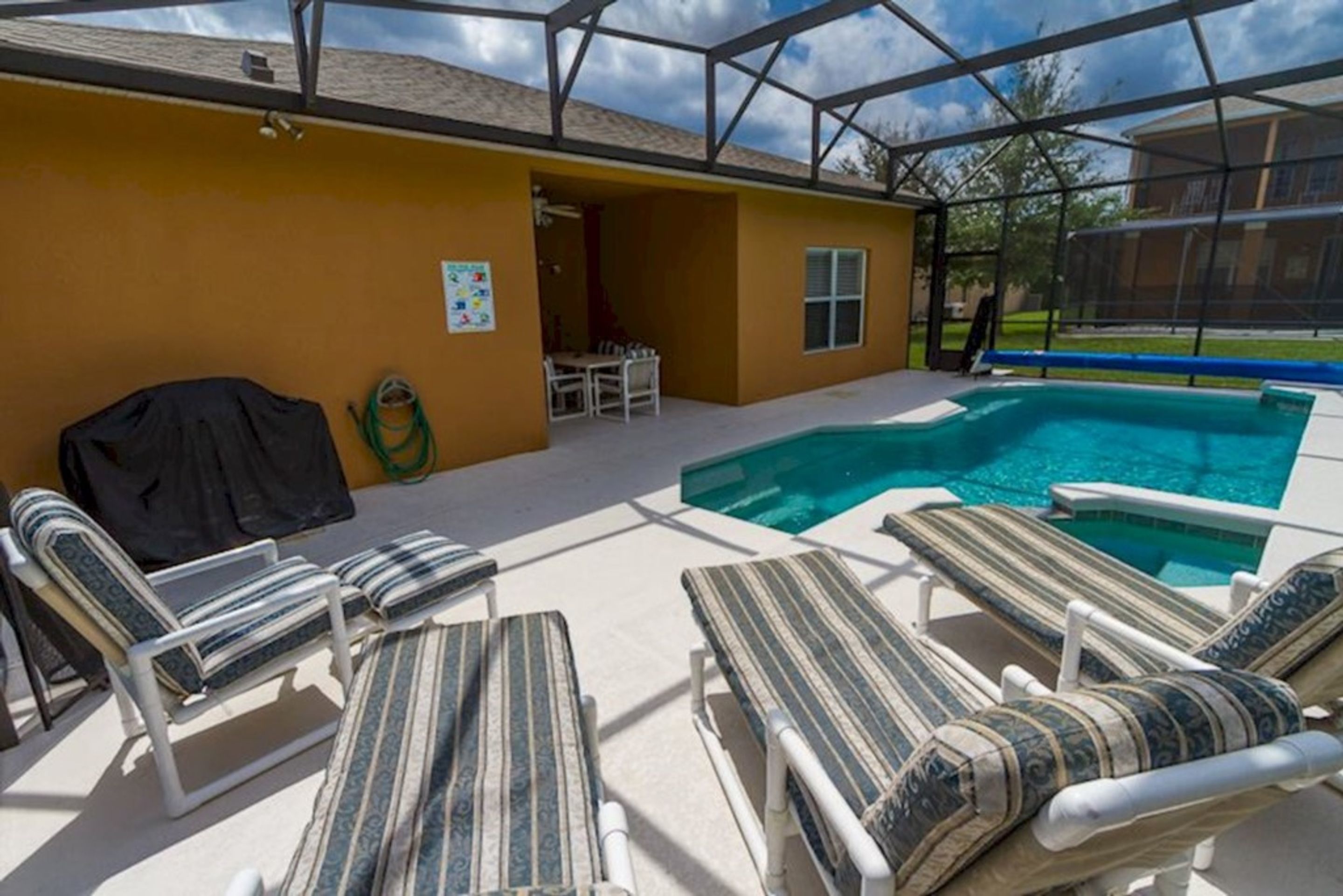 Uma área externa coberta com piscina, espreguiçadeiras e churrasqueira.