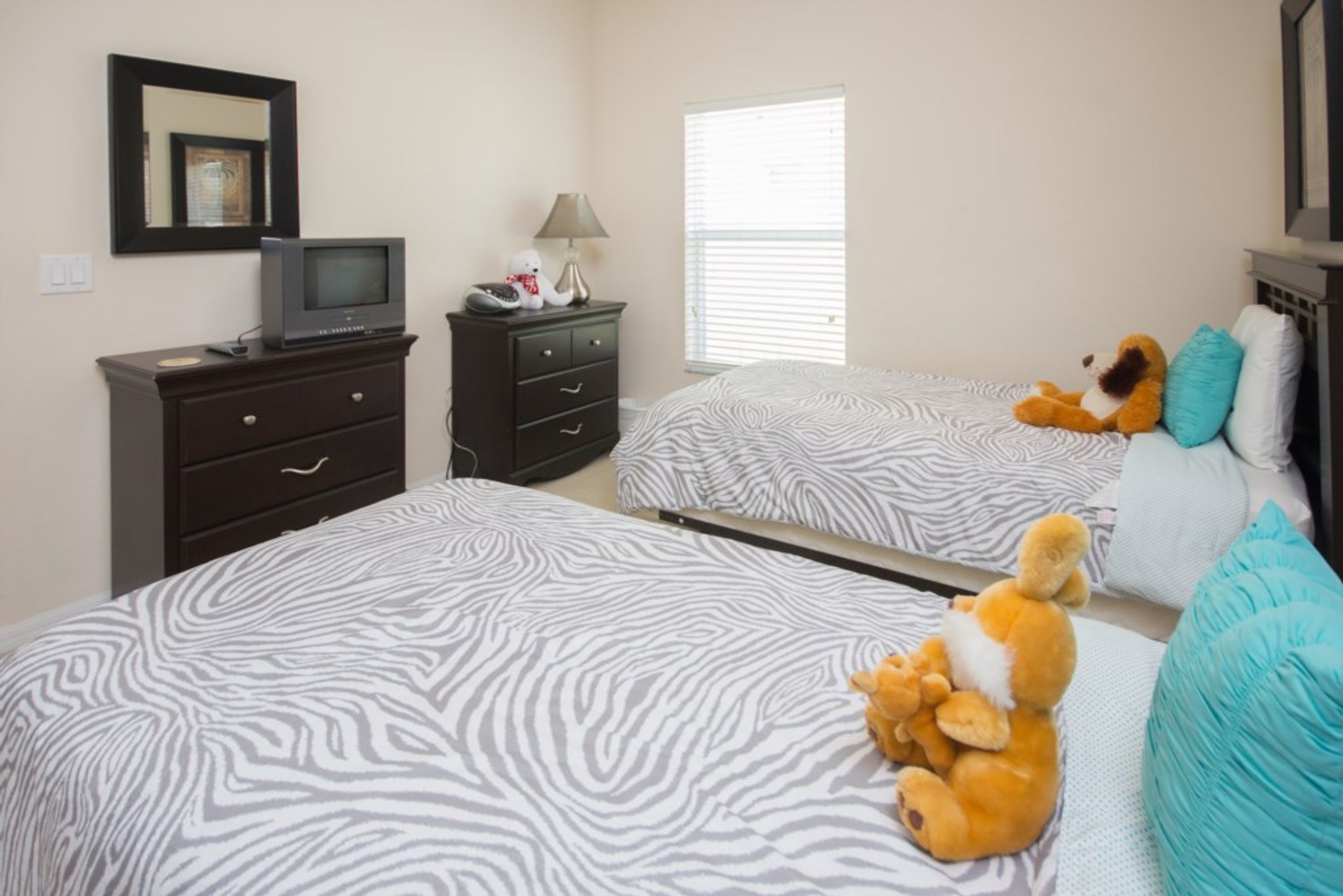 Un dormitorio con dos camas, un aparador, un televisor y peluches.