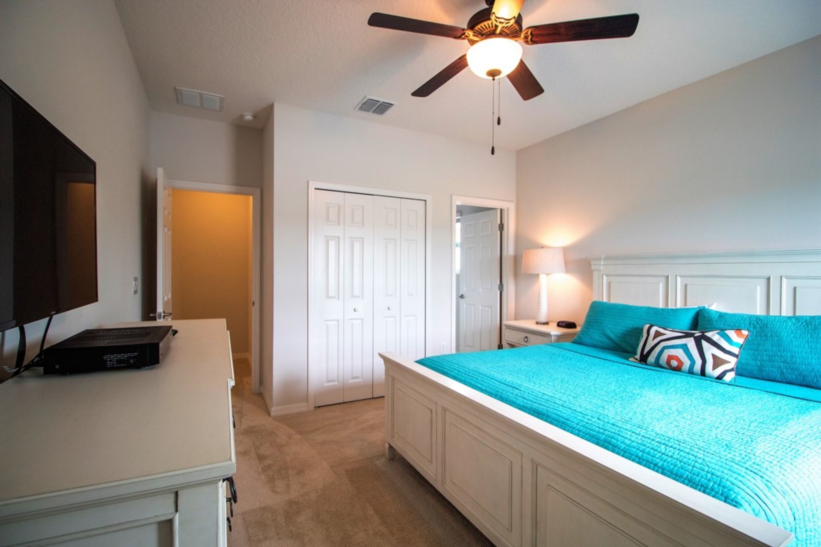 A bedroom with a bed, a ceiling fan, a desk, and a TV.