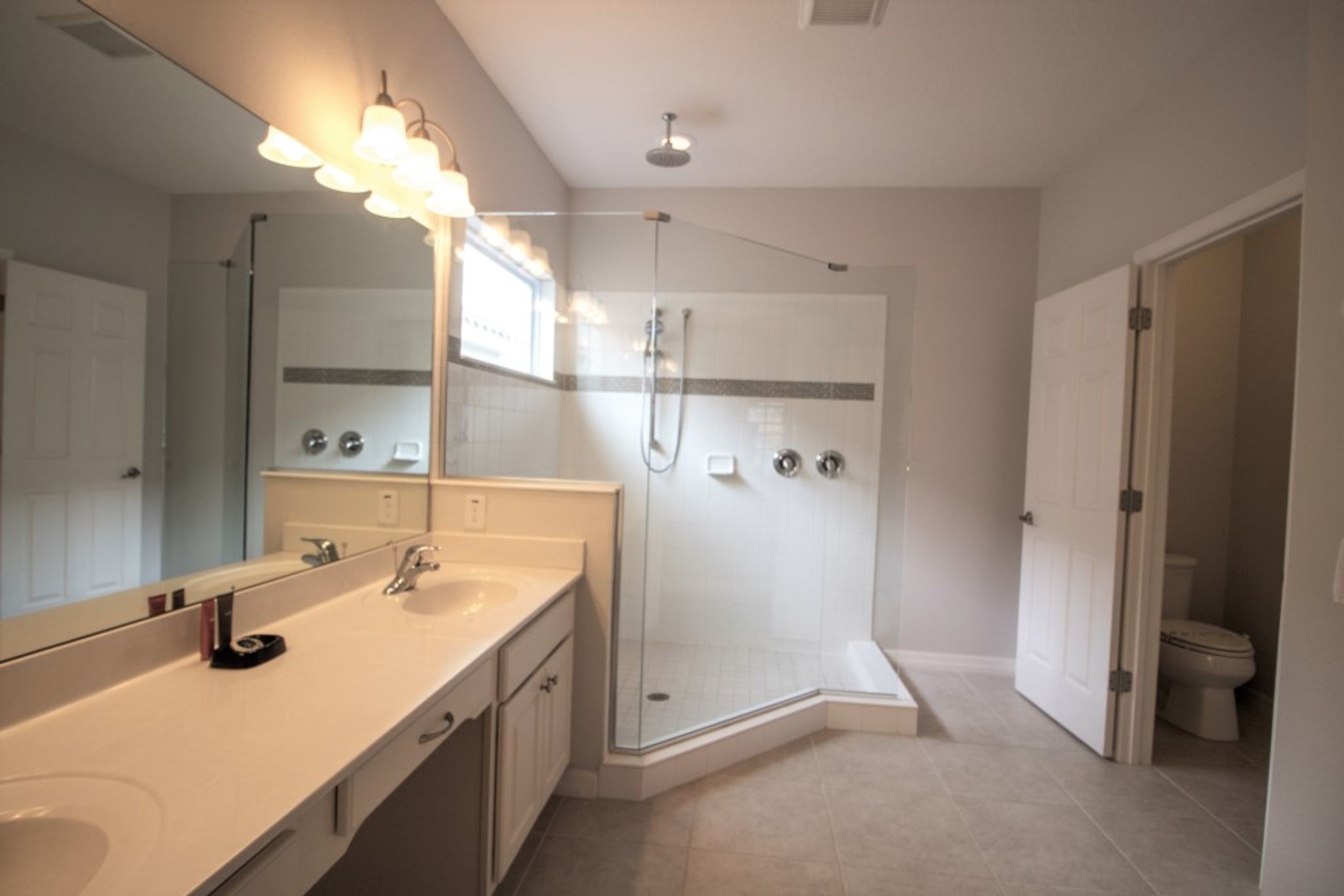 A modern bathroom with a large mirror, a sink, a shower enclosure, and a toilet.