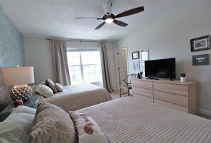 A hotel room with two beds, a ceiling fan, a TV, a dresser, and a window with curtains. - Storey Lake 4764 (Kissimmee)