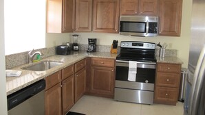A kitchen with wooden cabinets, stainless steel appliances, a dishwasher, and a granite countertop. - Indian Wells 3181 (Kissimmee)