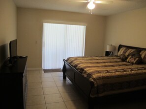A bedroom with a bed, a desk, a chair, a ceiling fan, and a window with blinds.