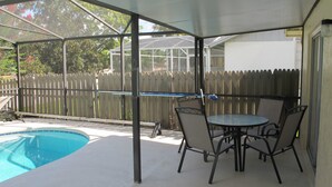 A covered patio with a pool, a table with chairs, and a wooden fence in the background. - Indian Wells 3181 (Kissimmee)