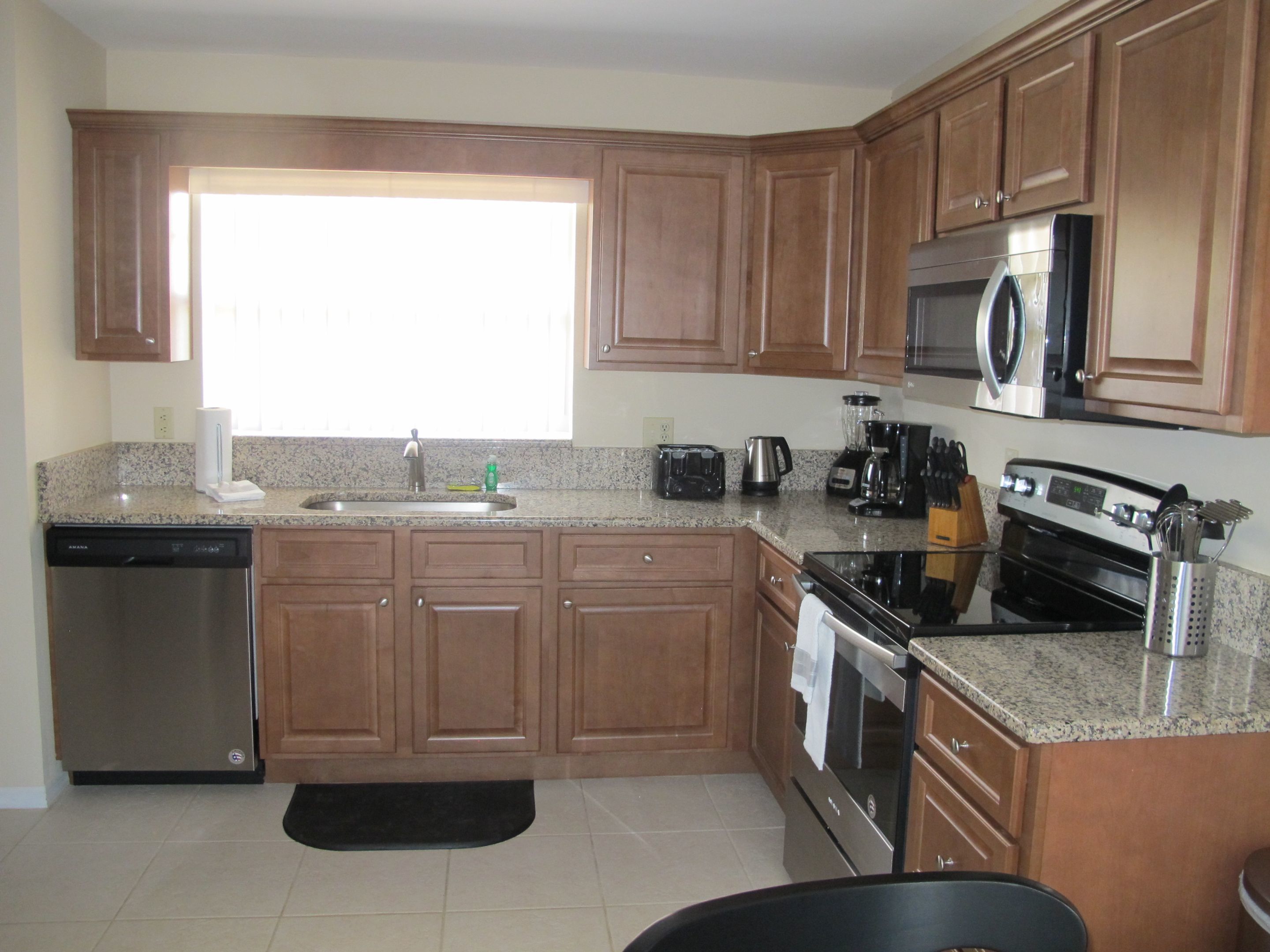 A kitchen with wooden cabinets, a dishwasher, a stove, a microwave, and a window.