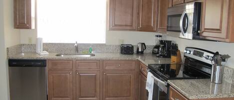 A kitchen with wooden cabinets, a dishwasher, a stove, a microwave, and a window.