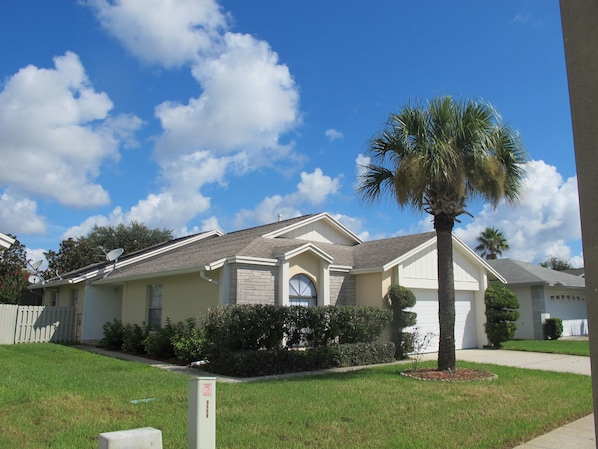 A single-story house with a gabled roof, a front porch, and a palm tree in the front yard.
