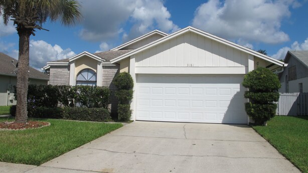 A residential house with a garage, a driveway, and a well-maintained lawn. - Indian Wells 3181 (Kissimmee)