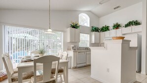 Una cocina luminosa con armarios blancos, un comedor con mesa y sillas, y un amplio ventanal que proporciona luz natural.
