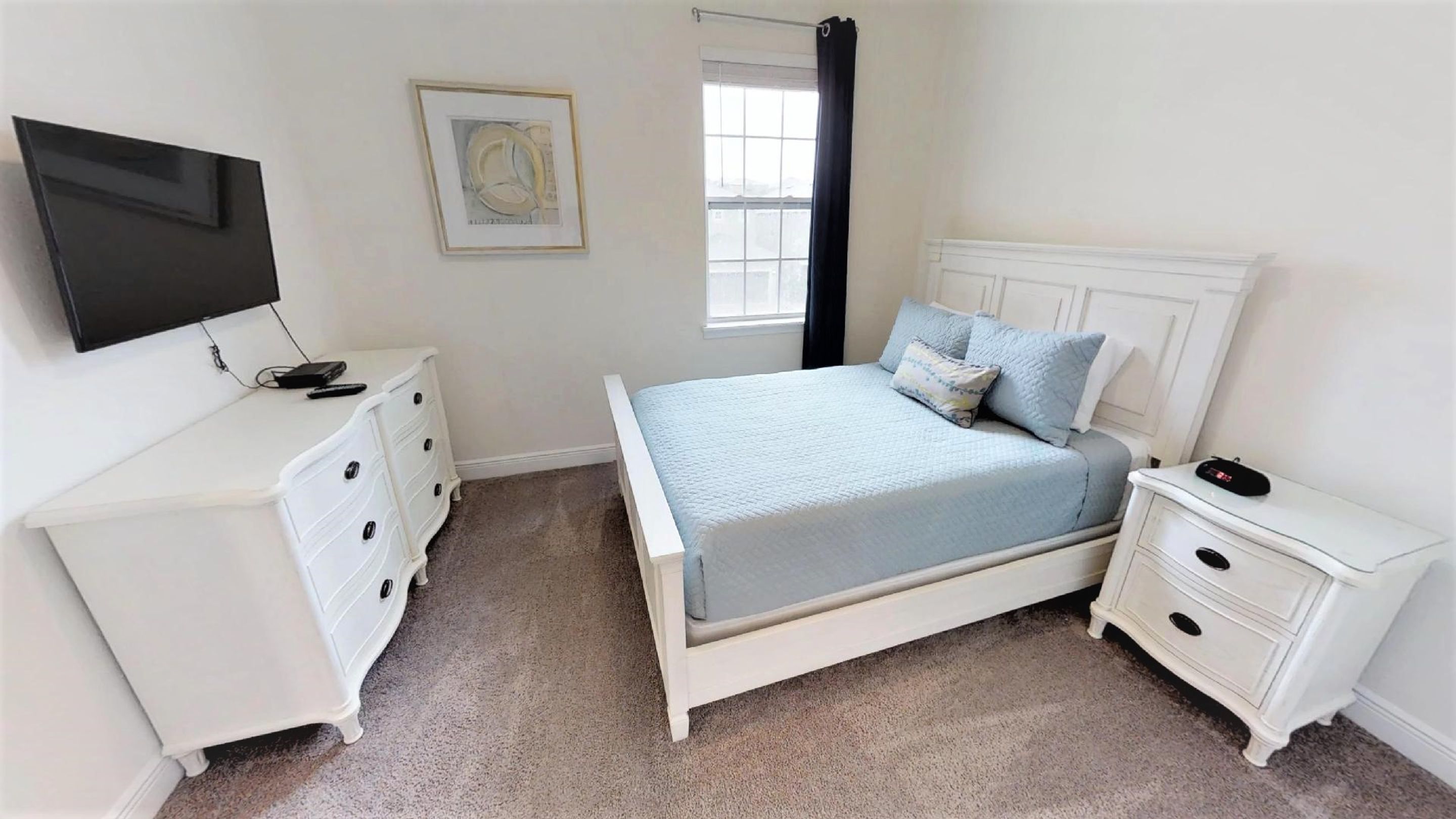 A bedroom with a bed, two nightstands, a dresser, a TV, a window with curtains, and a framed picture on the wall.