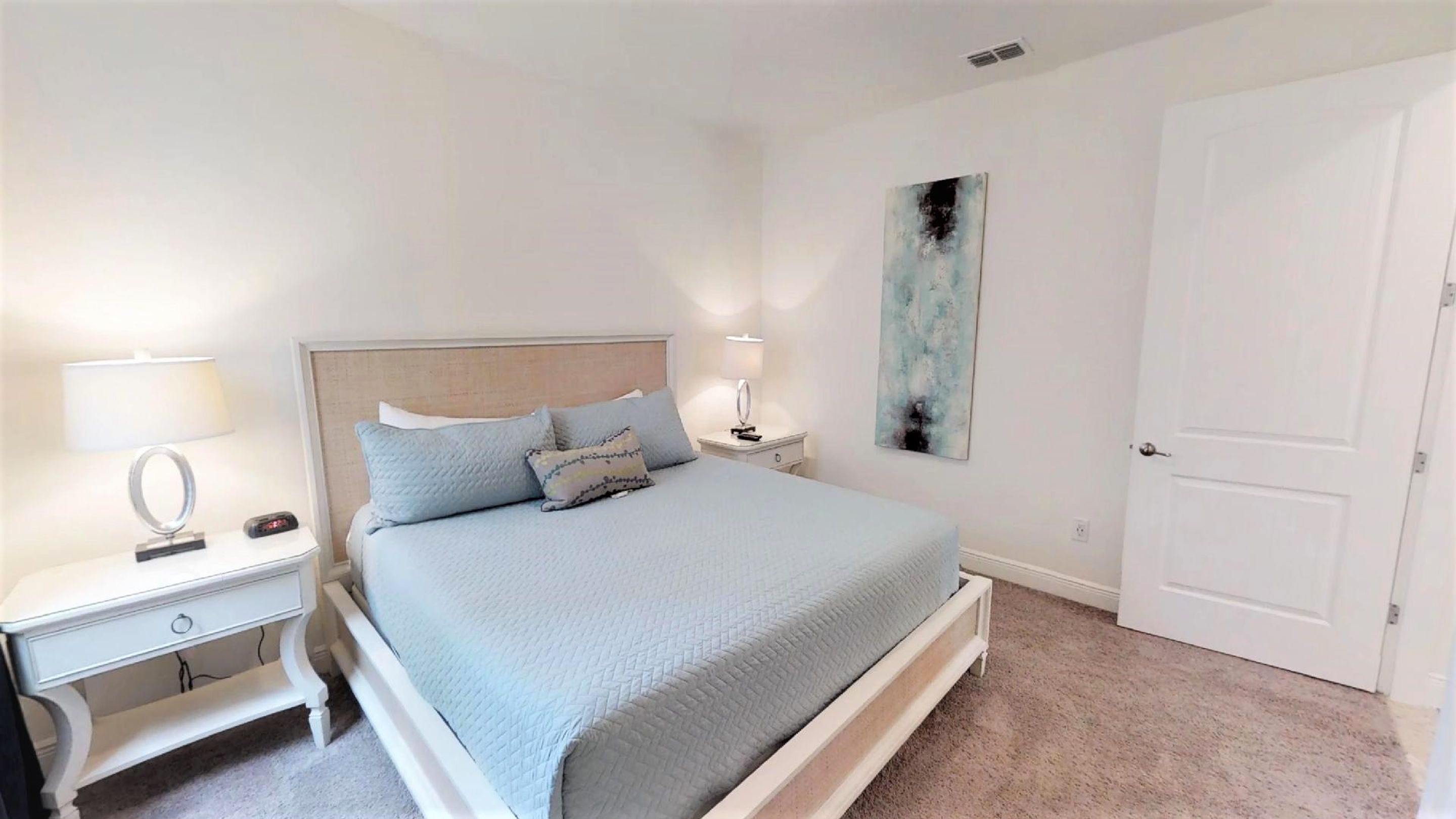 A bedroom with a bed, two bedside tables, a nightstand, a wall-mounted lamp, and a door.