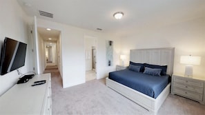 Un dormitorio con cama, mesitas de noche, televisor y puerta que da a otra habitación.