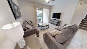 A modern living room with a sofa, a coffee table, a TV, and a staircase. - Encore Resort at Reunion 331 (Kissimmee)