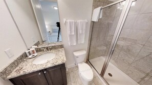 Un baño moderno con encimera de granito, inodoro y ducha con mampara de vidrio.