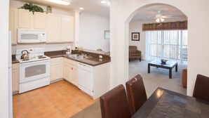 A compact kitchen with white cabinets, a microwave, stove, and dishwasher. There is a dining area with a table and chairs, and a view of a balcony through a window. - Palisades Resort 14200 - 409 (Winter Garden)