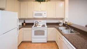 A kitchen with white cabinets, a white stove, a microwave, a dishwasher, and a granite countertop. - Palisades Resort 14200 - 409 (Winter Garden)