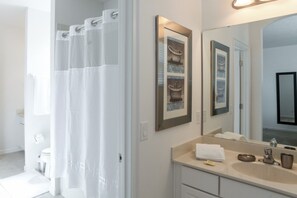 A modern bathroom with a shower curtain, a sink with a mirror, and framed artwork on the wall. - Solterra 5240 (Davenport)
